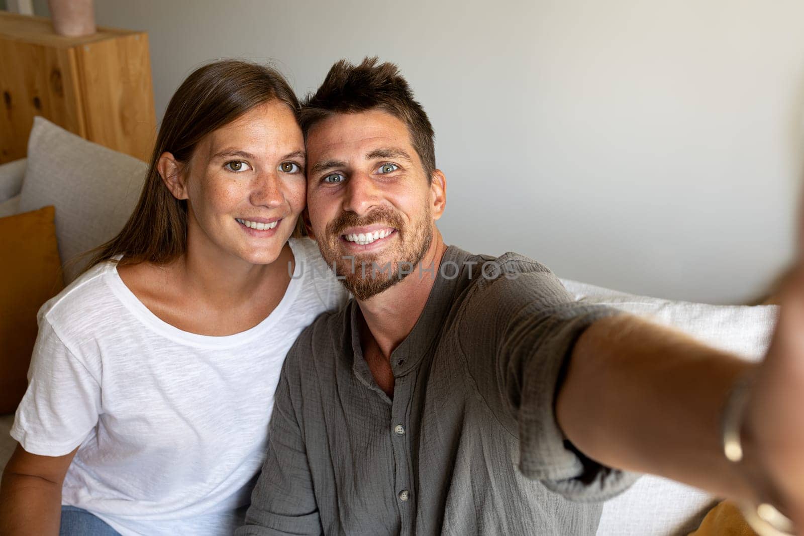 Young couple taking selfie relaxing sitting on the sofa looking at camera. Lifestyle and technology.
