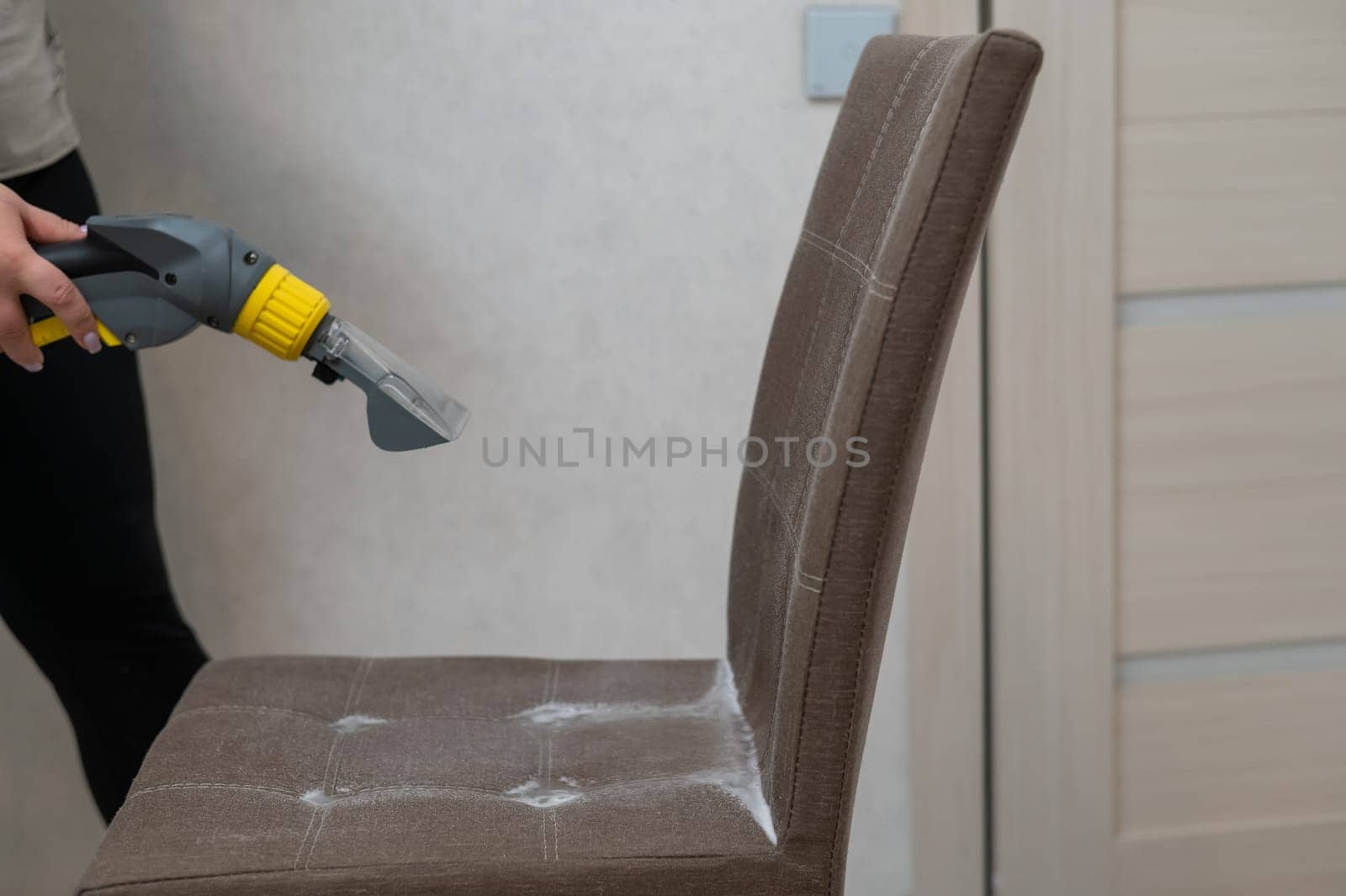 Woman cleaning a fabric chair with a professional washing vacuum cleaner