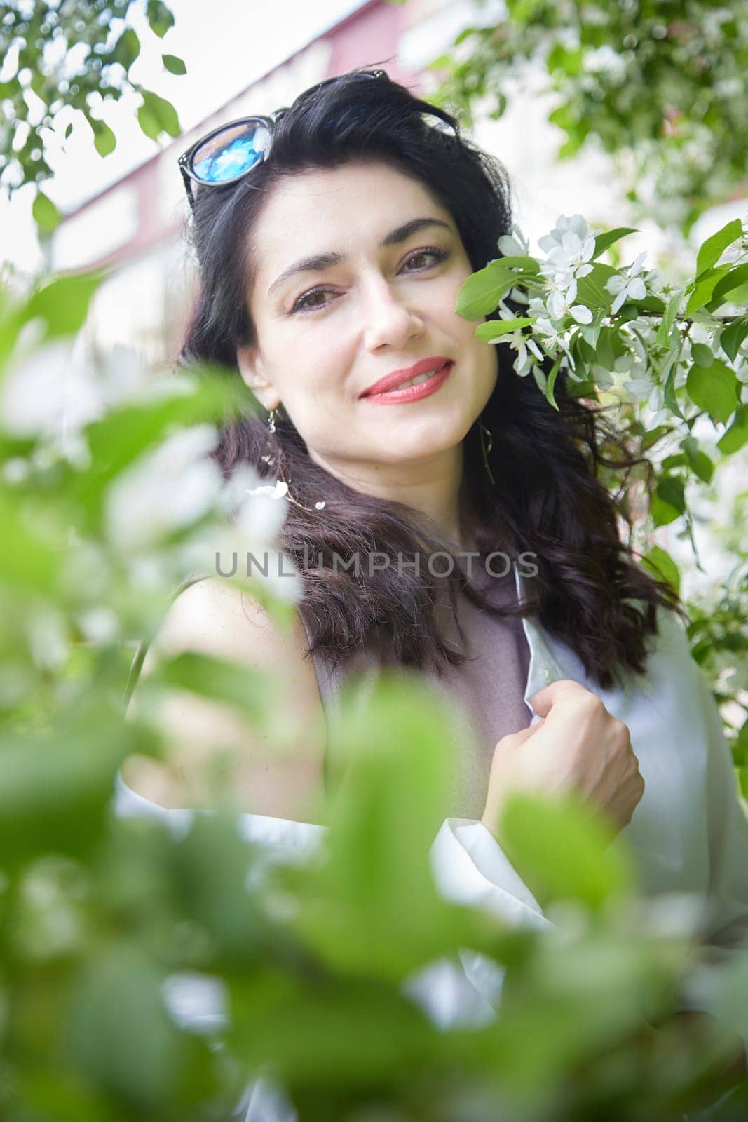 Joyous brunette woman near Blossoms of apple tree in a Spring Garden outdoors. The Concept of face and body care. The scent of perfume and tenderness