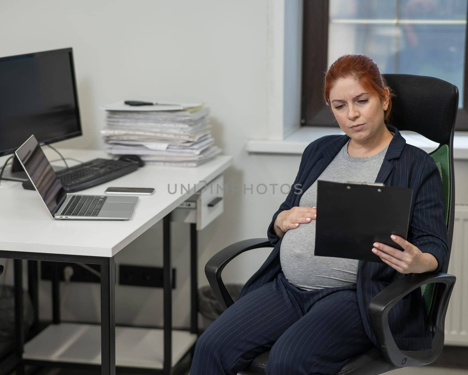 Pregnant woman reading documents on a paper tablet in the office. by mrwed54