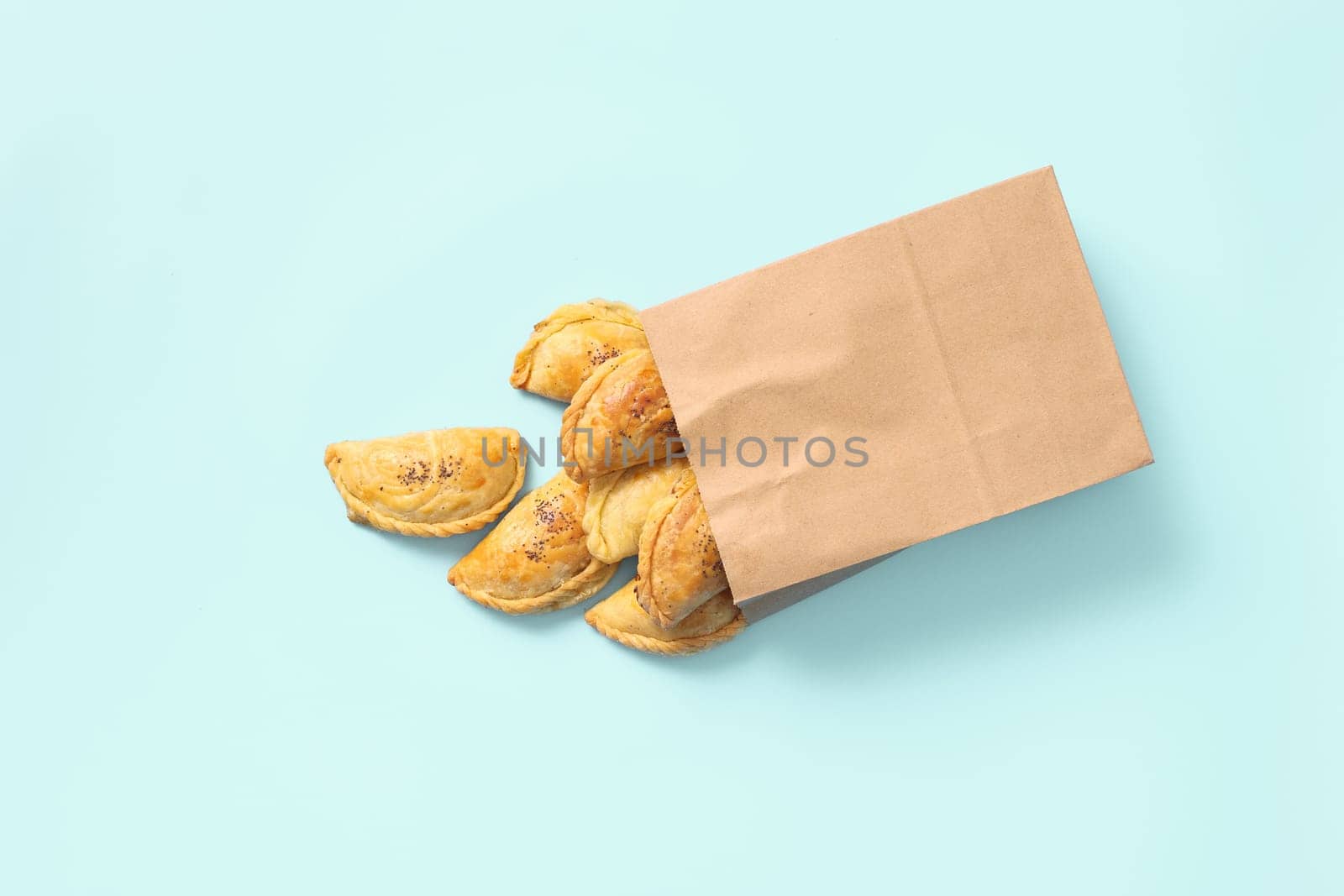 Delightful Food Delivery: Samsa Pies Sprinkled with Poppy Seeds in Paper Bag on Blue Background.