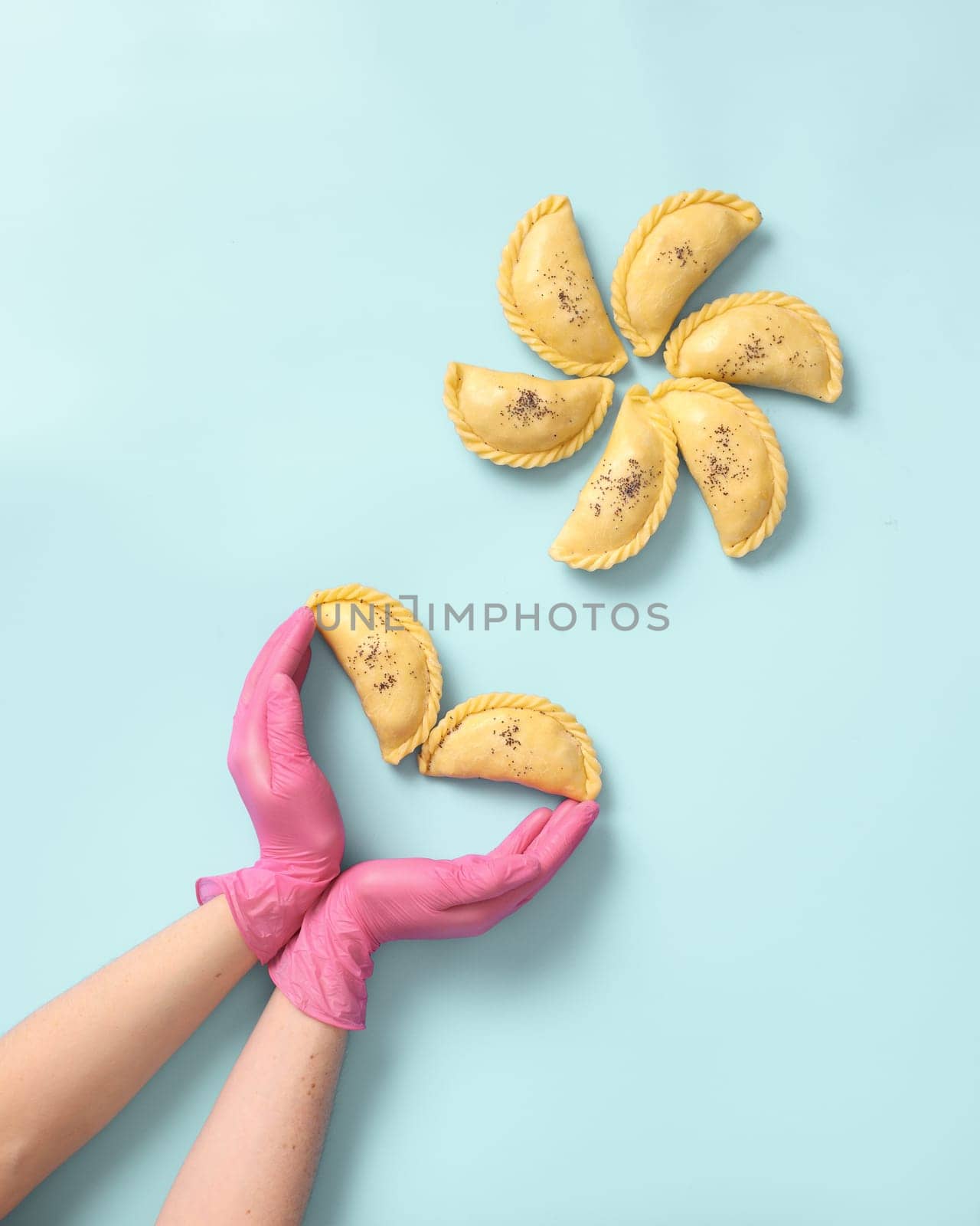Top view a woman baker's hands in a rubber gloves lays out raw samsa on blue background. Traditional indian cuisine, frozen semi-finished products.