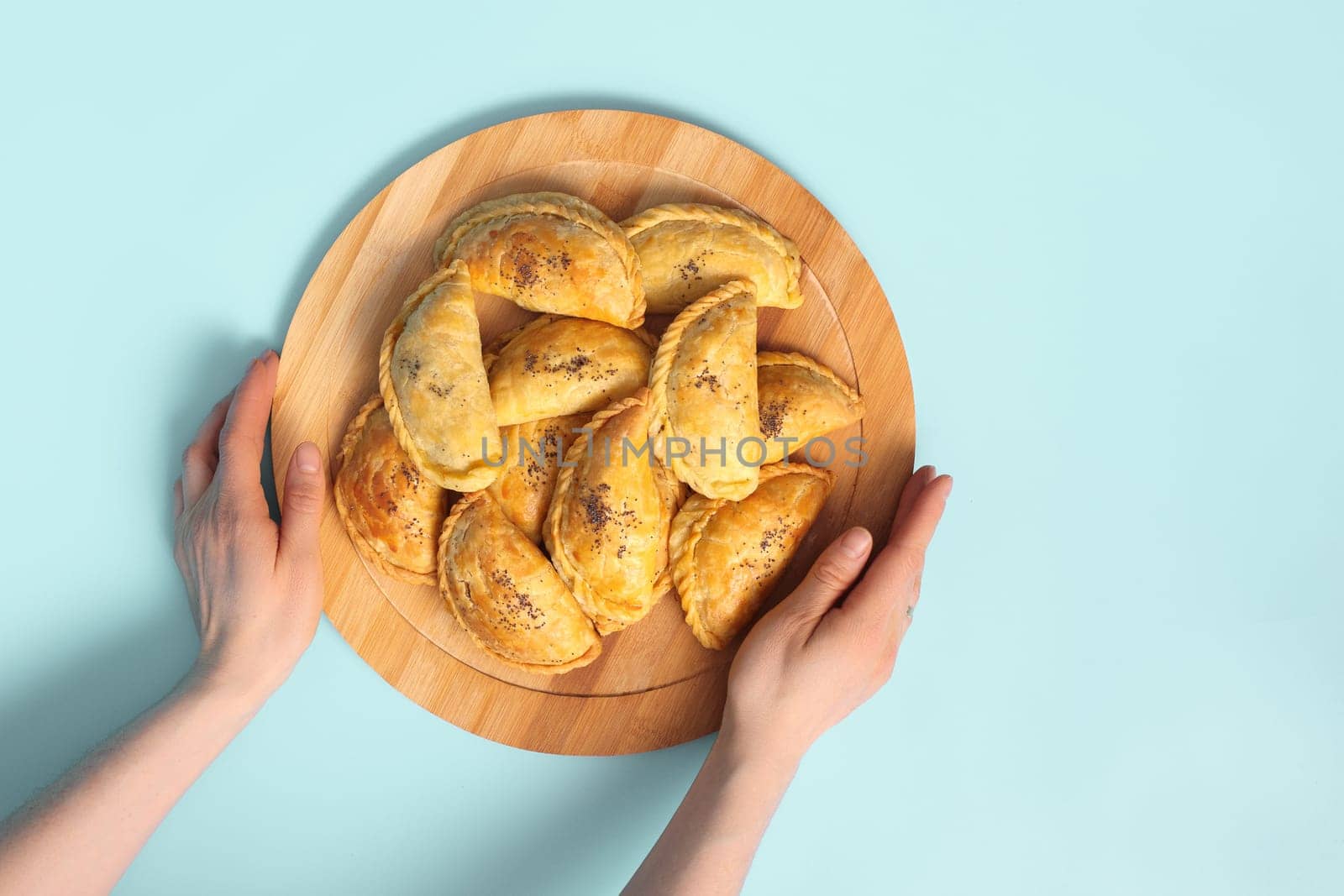 Top view on woman hands with wooden plate with baked samsa pies on blue background.