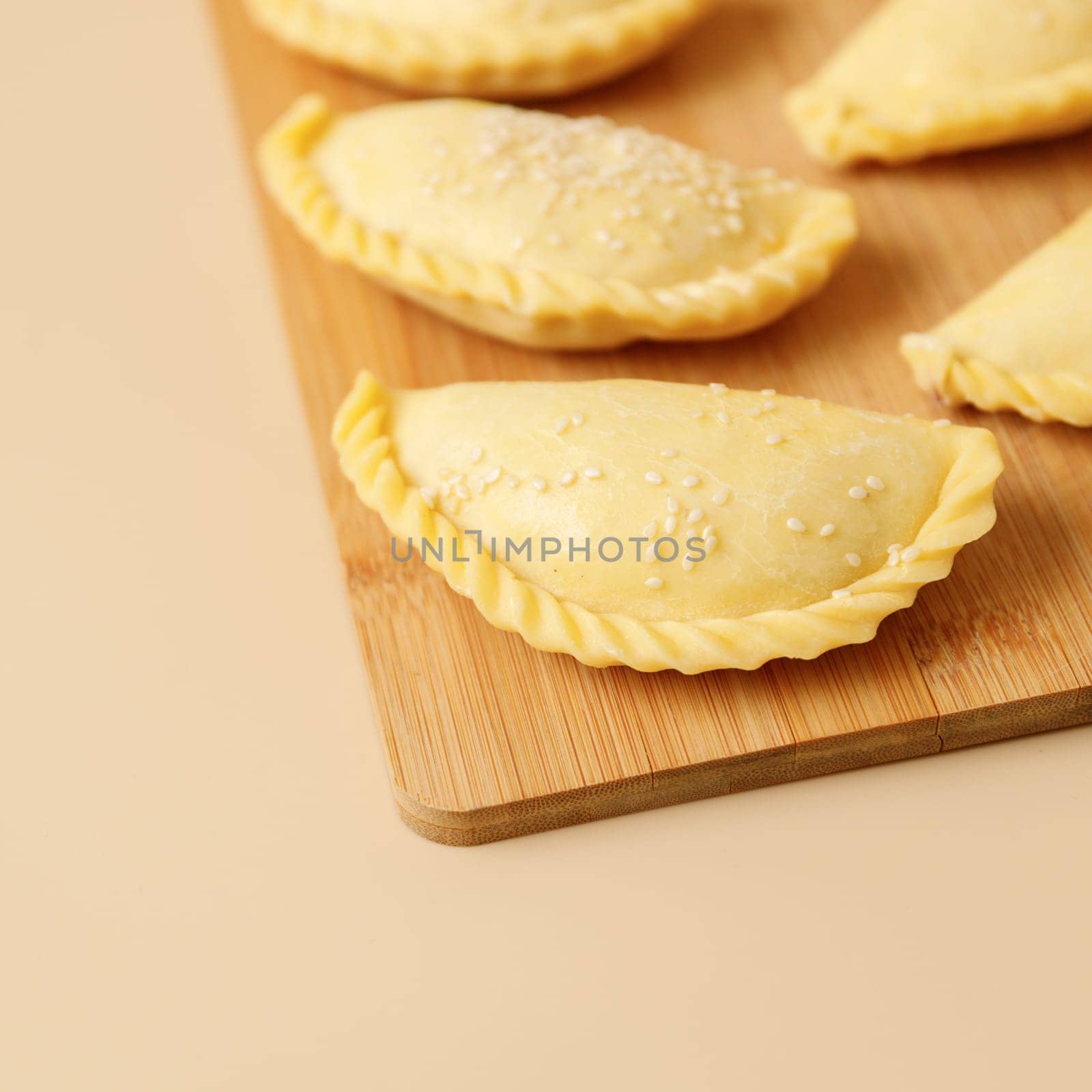 Close-up raw vegetable samsa with sesame on a wooden board . Traditional Indian cuisine, frozen semi-finished products.