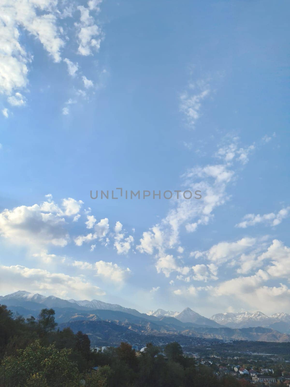 Natural vertical landscape with a clear blue sky filled with fluffy white cumulus clouds, showcasing a stunning ecoregion of highland grasslands and majestic Almaty mountains in the background.