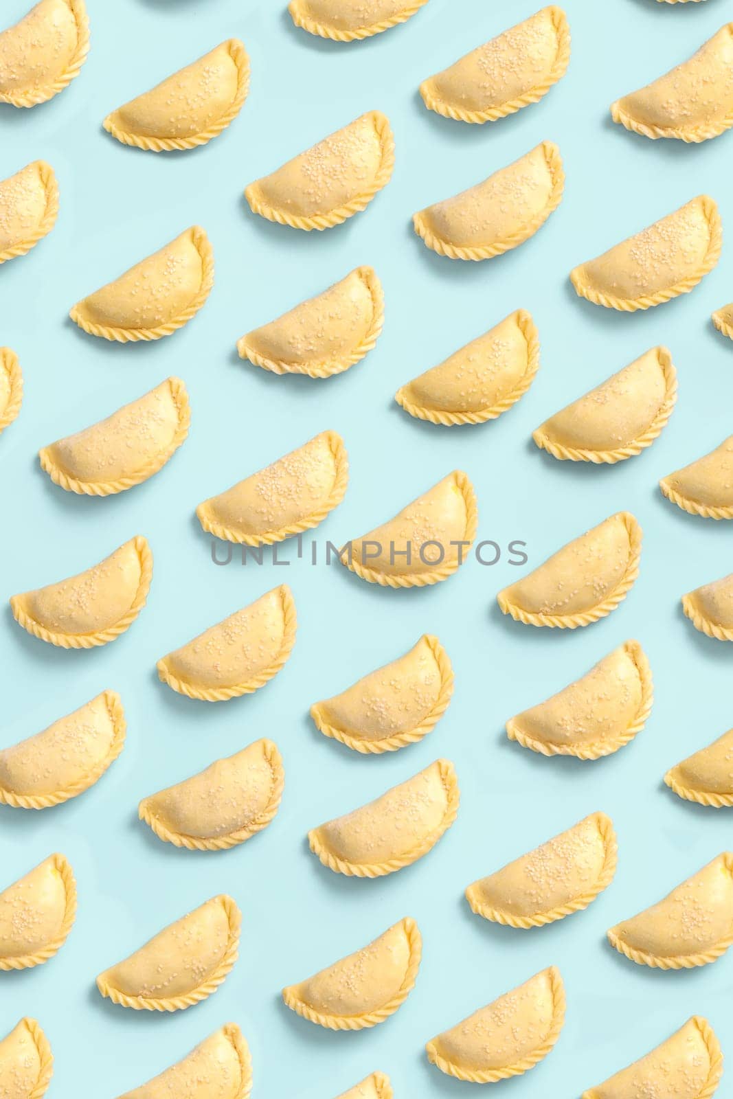 Top view on raw pies or samsa or samosas on blue background, frozen semi-finished products, bakery background.