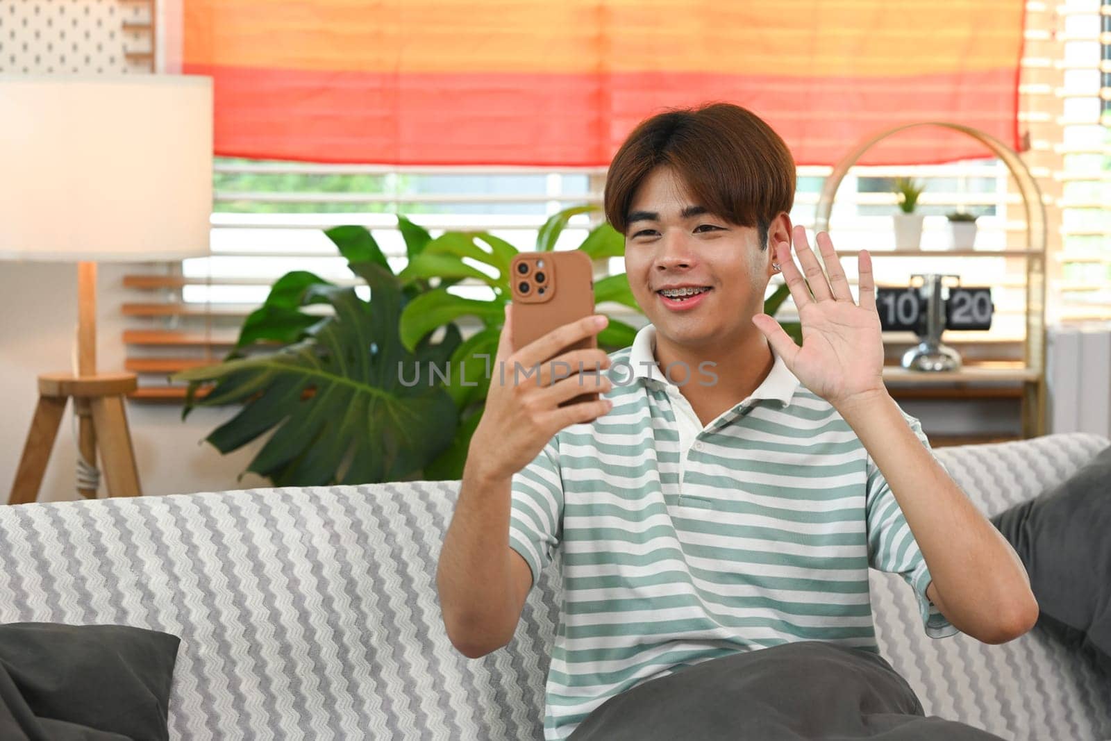 Cheerful young man making video call on mobile phone sitting on sofa at home.