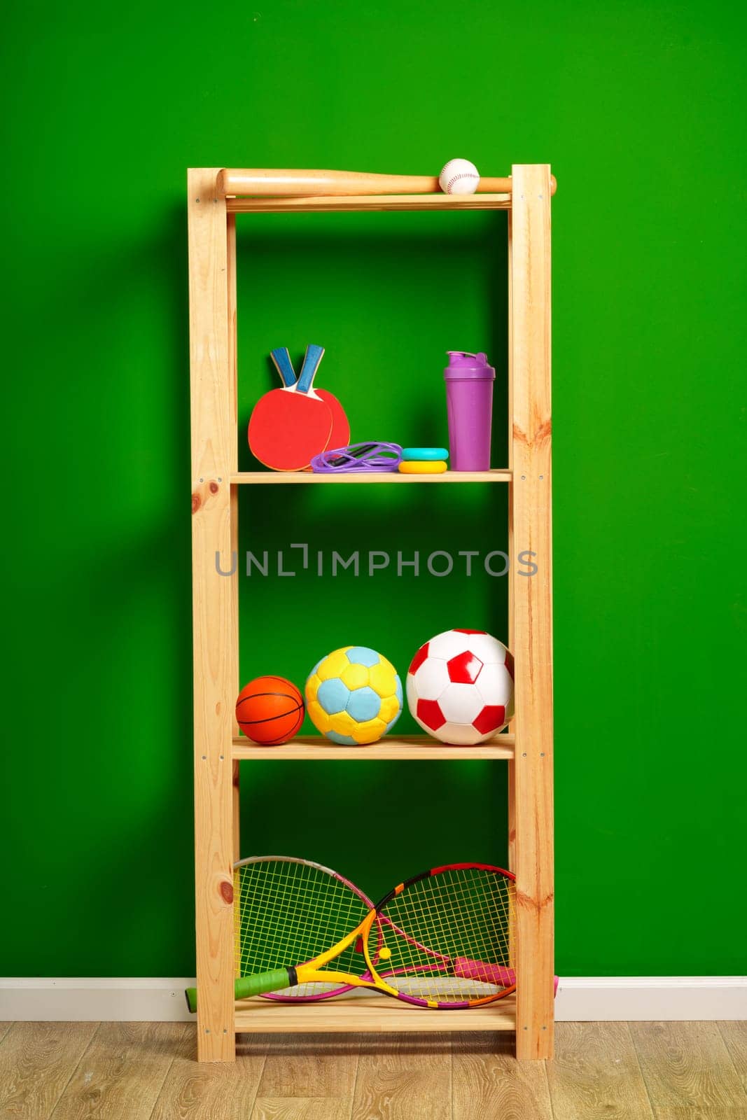 Shelves with different sports equipment against green wall close up