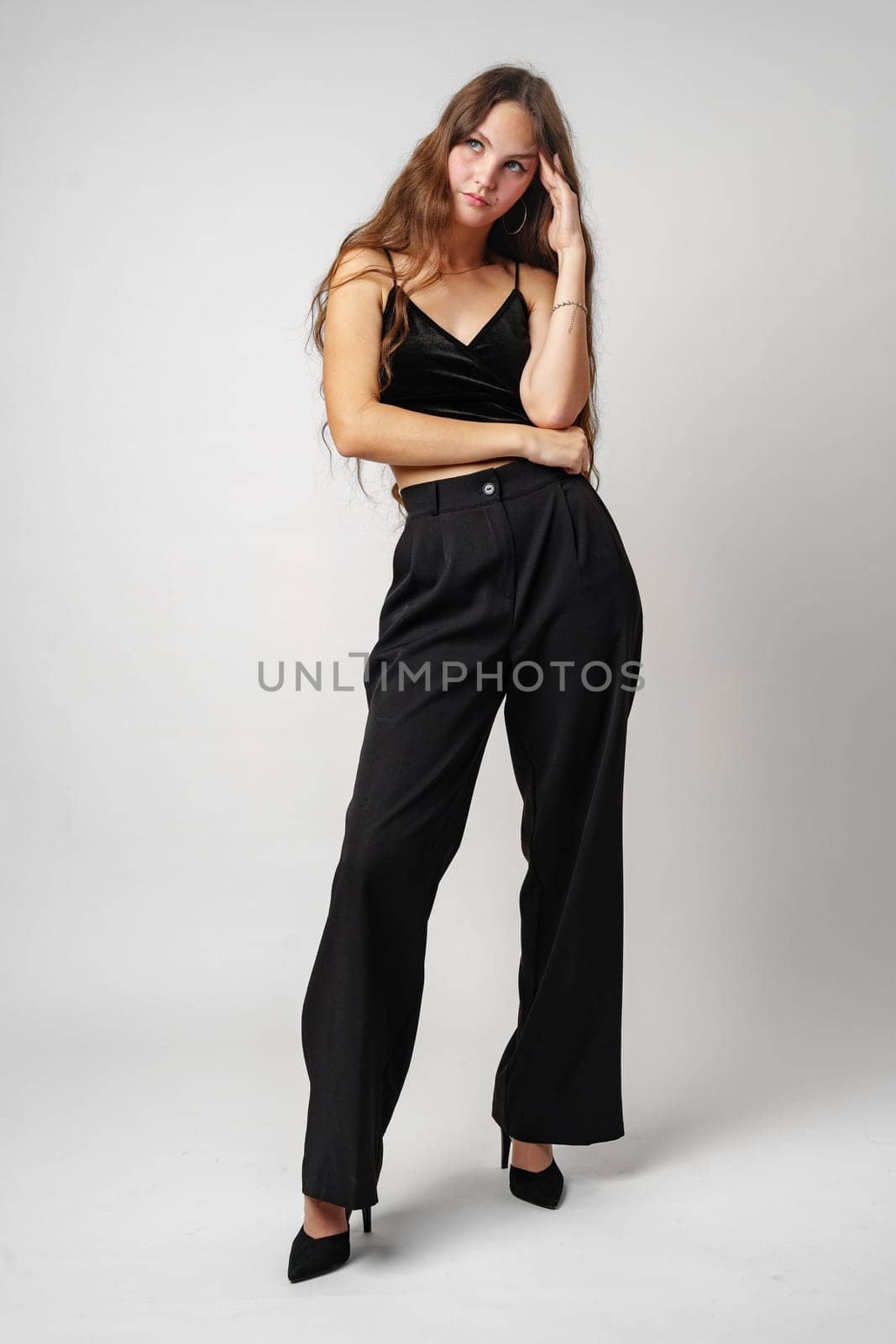 A woman wearing a black top and black pants stands in a neutral pose against a plain background. Her outfit is simple and stylish, adding a touch of elegance to her appearance.