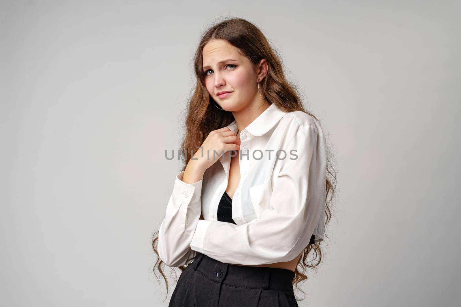 A woman stands wearing a white shirt and black pants. She is posing for the camera in a casual outfit, exuding confidence and style.