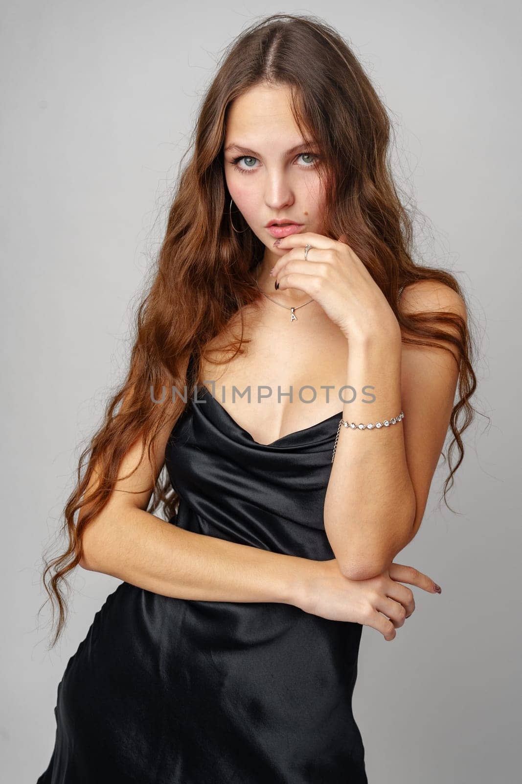 A woman wearing a black dress strikes a pose for a photograph, looking elegant and stylish in her attire. The backdrop is simple, allowing her to be the focal point of the image.