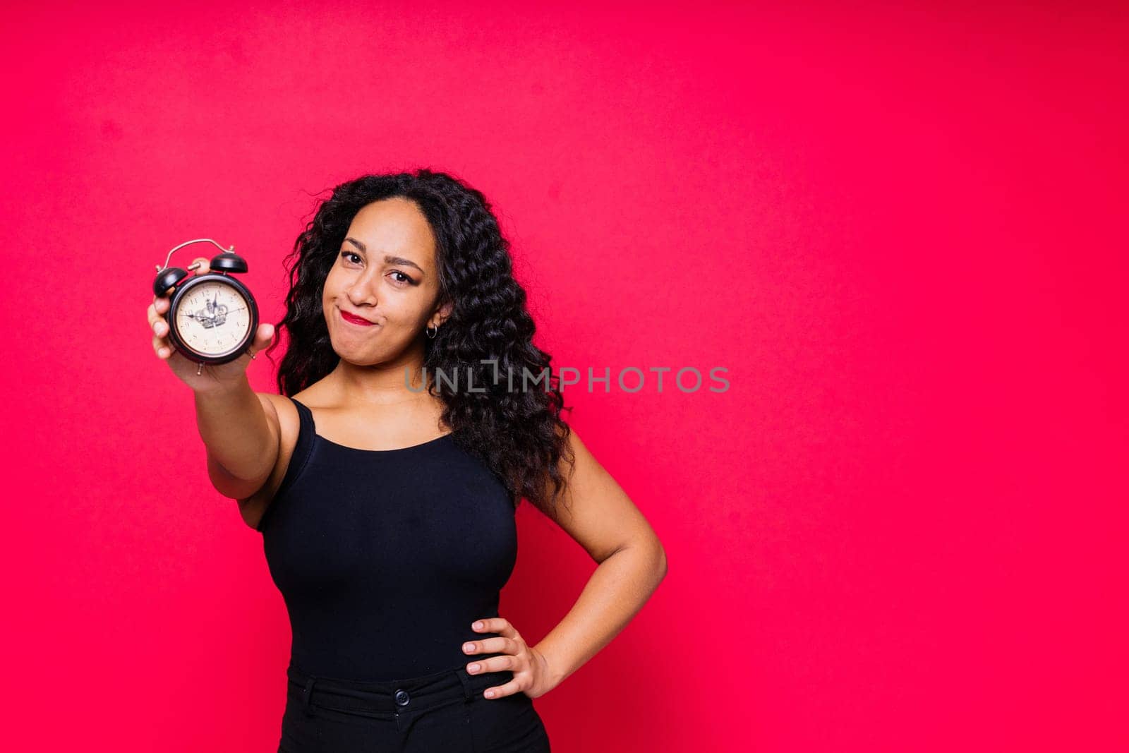 Smiling young african american woman posing isolated on a red background with clock