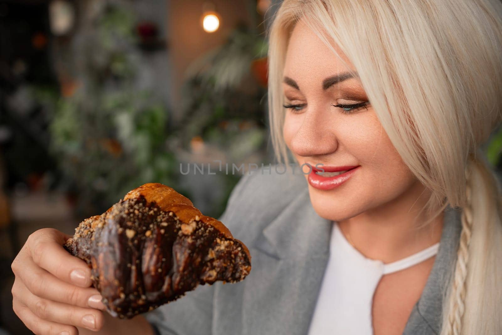 A blonde woman is eating a chocolate pastry. She is smiling and she is enjoying her treat