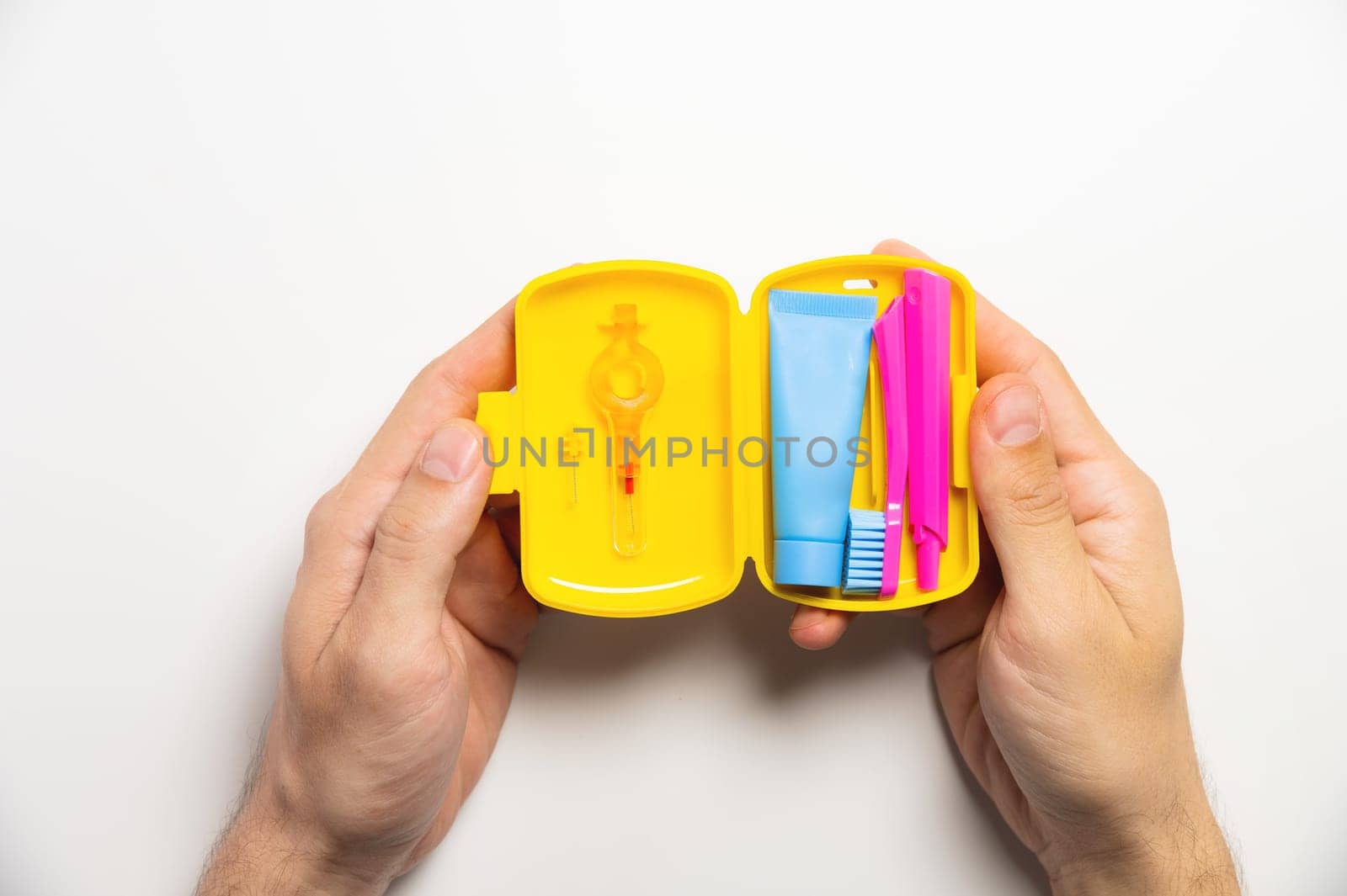 Dental hygiene and oral care products in a yellow travel cosmetic bag on a white background with copy space in a man's hand. Flat lay, top view composition.