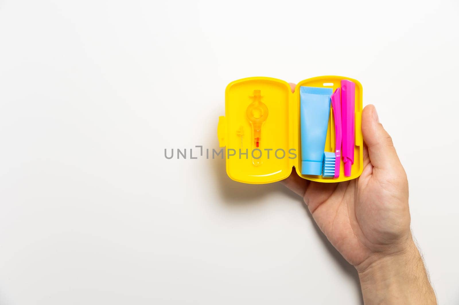 Dental hygiene and oral care products in a yellow travel cosmetic bag on a white background with copy space in a man's hand. Flat lay, top view composition by yanik88