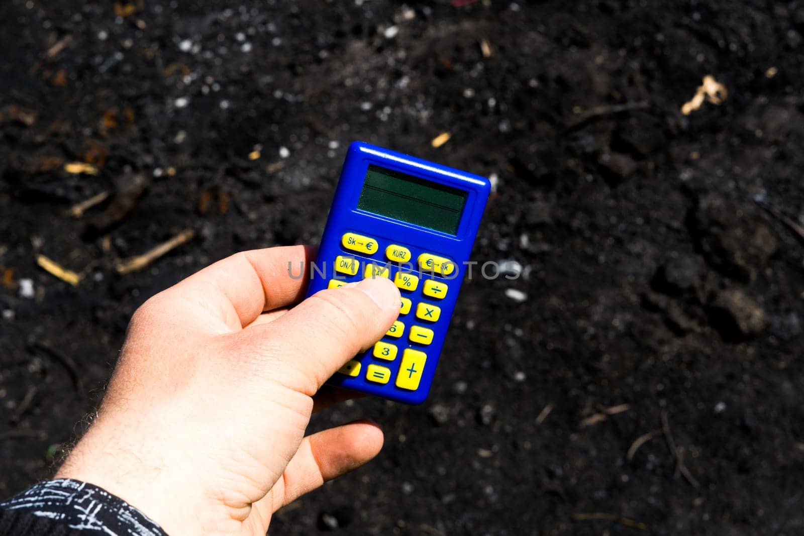 Blue calculator in dark soil, burnt ground after the fire by Zelenin