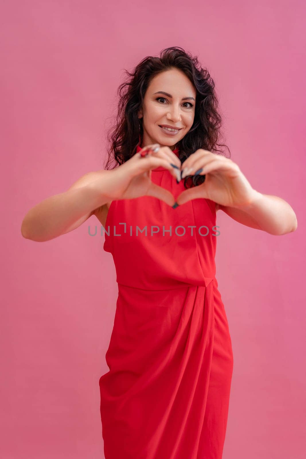 A woman in a red dress is smiling and holding her hands together to make a heart shape. Concept of love and happiness