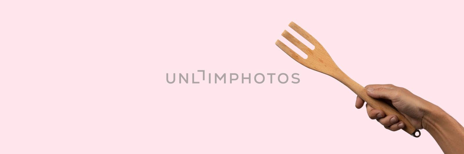 Hand holding wooden fork on pink background, cutout by TropicalNinjaStudio