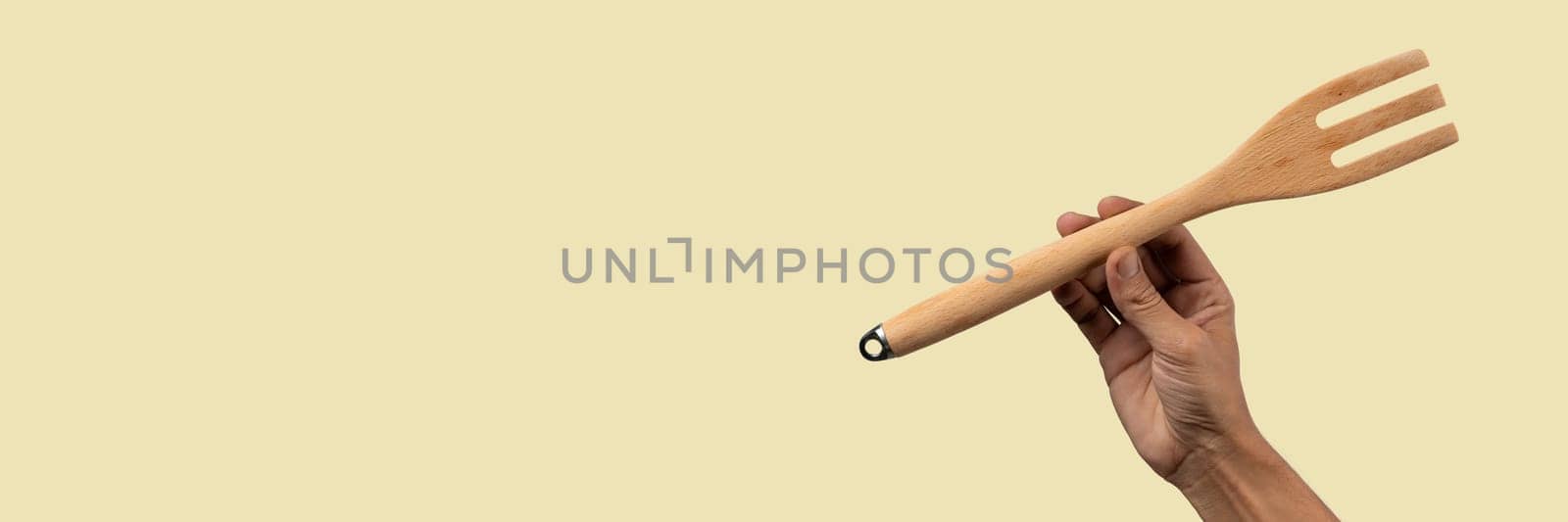 Hand holding wooden fork on beige background banner cutout. High quality photo