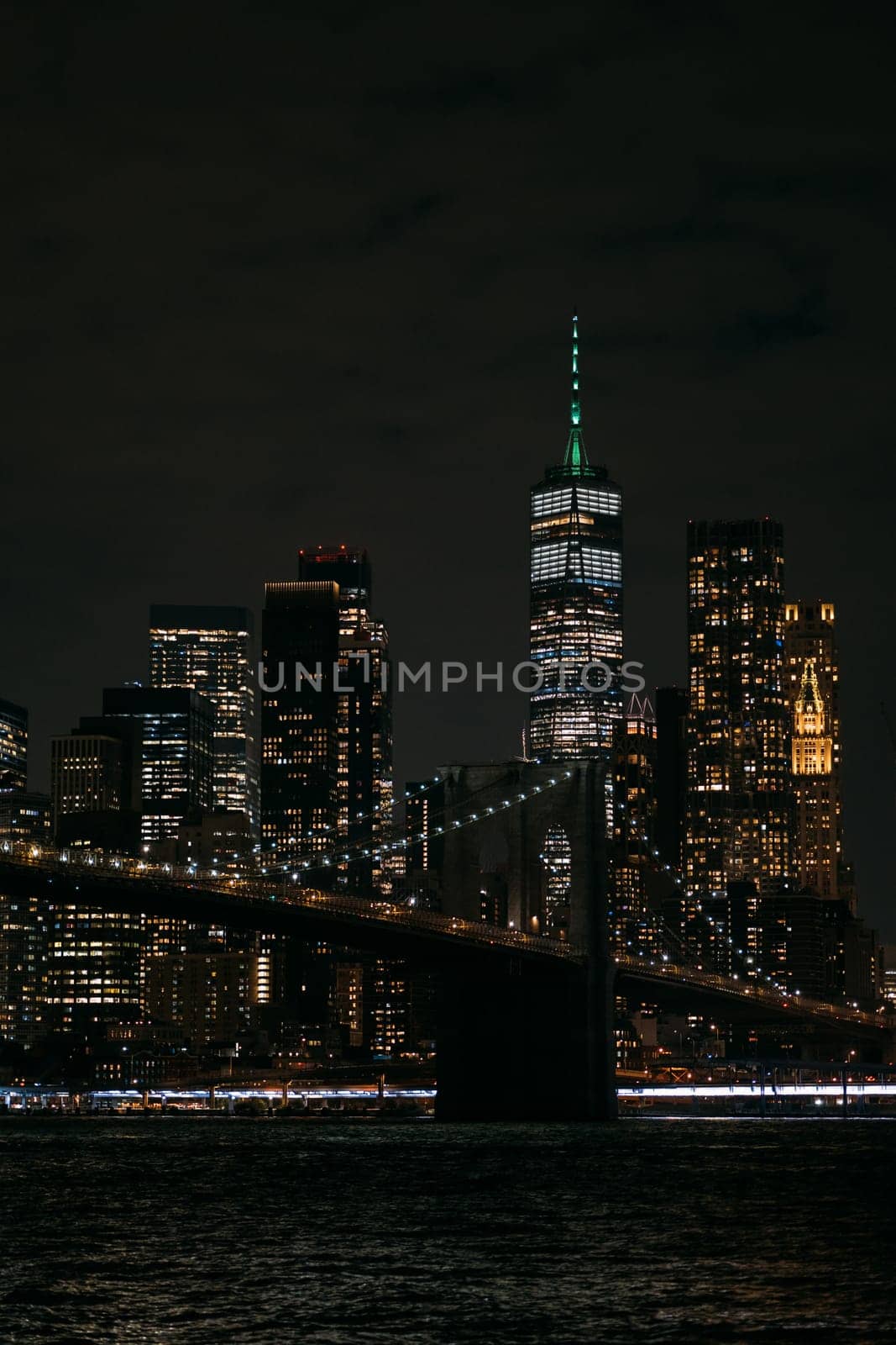 A stunning night view of the New York City skyline featuring the iconic Brooklyn Bridge and brightly lit skyscrapers. The image captures the vibrant, bustling atmosphere of the city after dark.