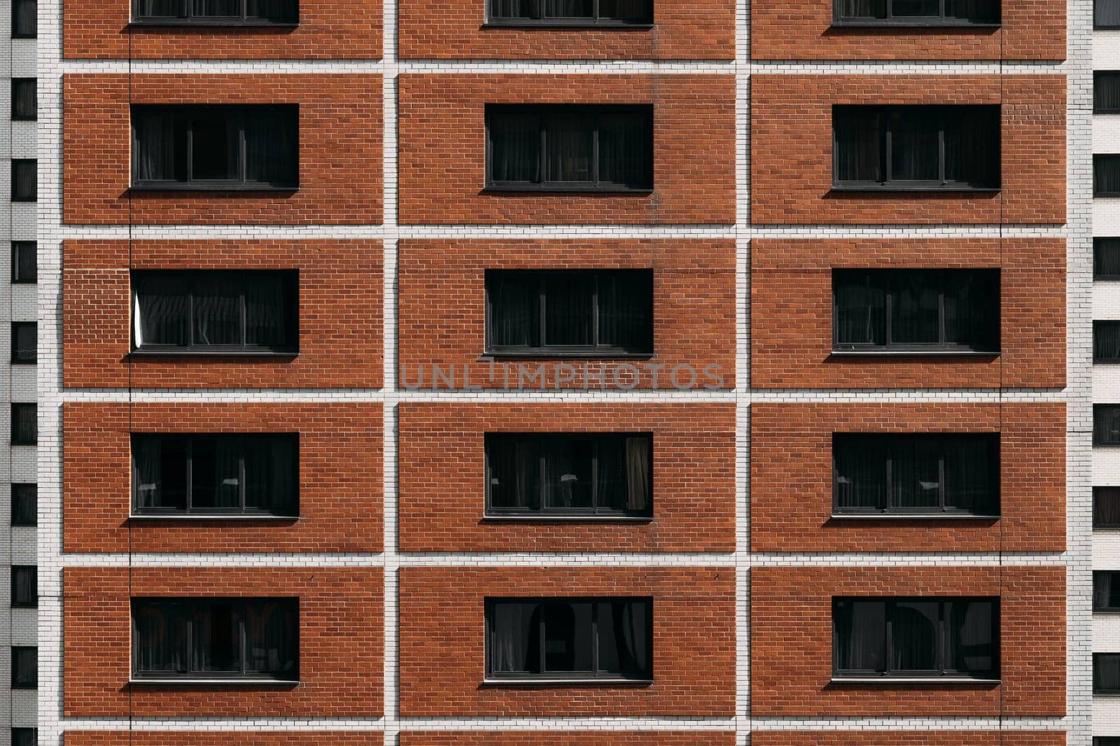 The symmetrical facade of a modern brick apartment building features rows of evenly spaced dark windows. The structure exhibits a blend of contemporary and traditional architectural elements.