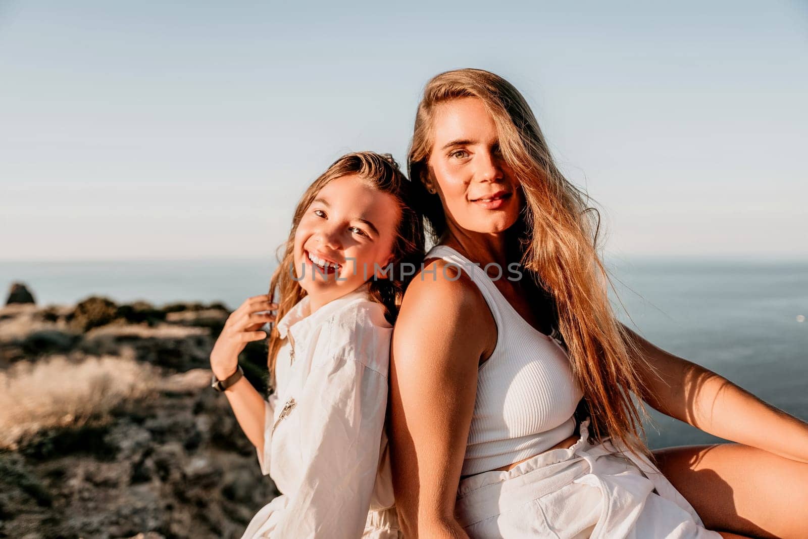 Close up portrait of mom and her teenage daughter hugging and smiling together over sunset sea view. Beautiful woman relaxing with her child.