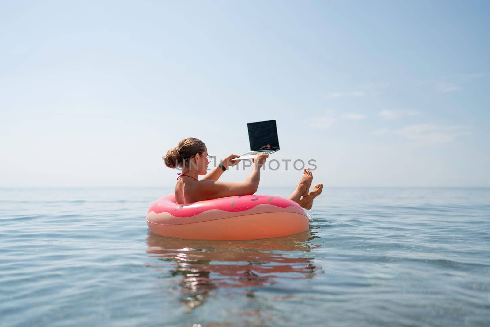 Woman laptop sea. Freelancer woman in sunglases floating on an inflatable big pink donut with a laptop in the sea. People summer vacation rest lifestyle concept