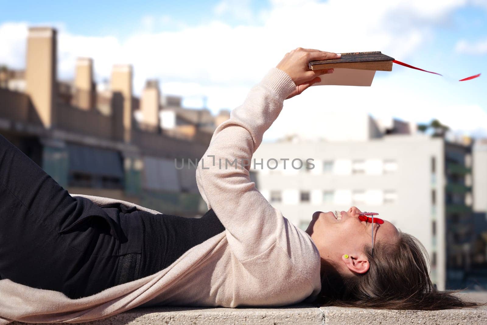 Young woman holding book up in air, low angle view outdoors by mariaphoto3