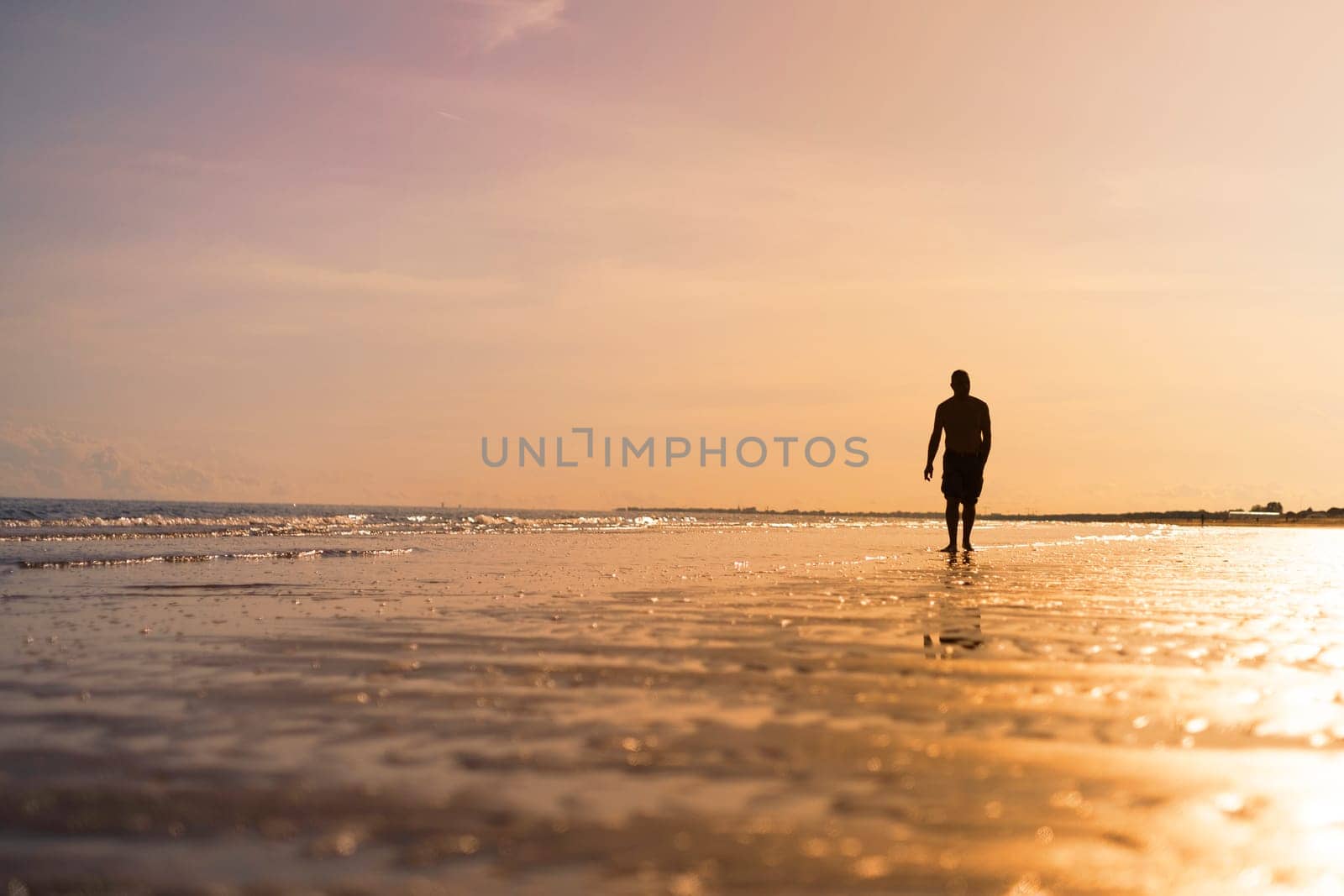 The silhouette of a man waking along the seashore at sunset.