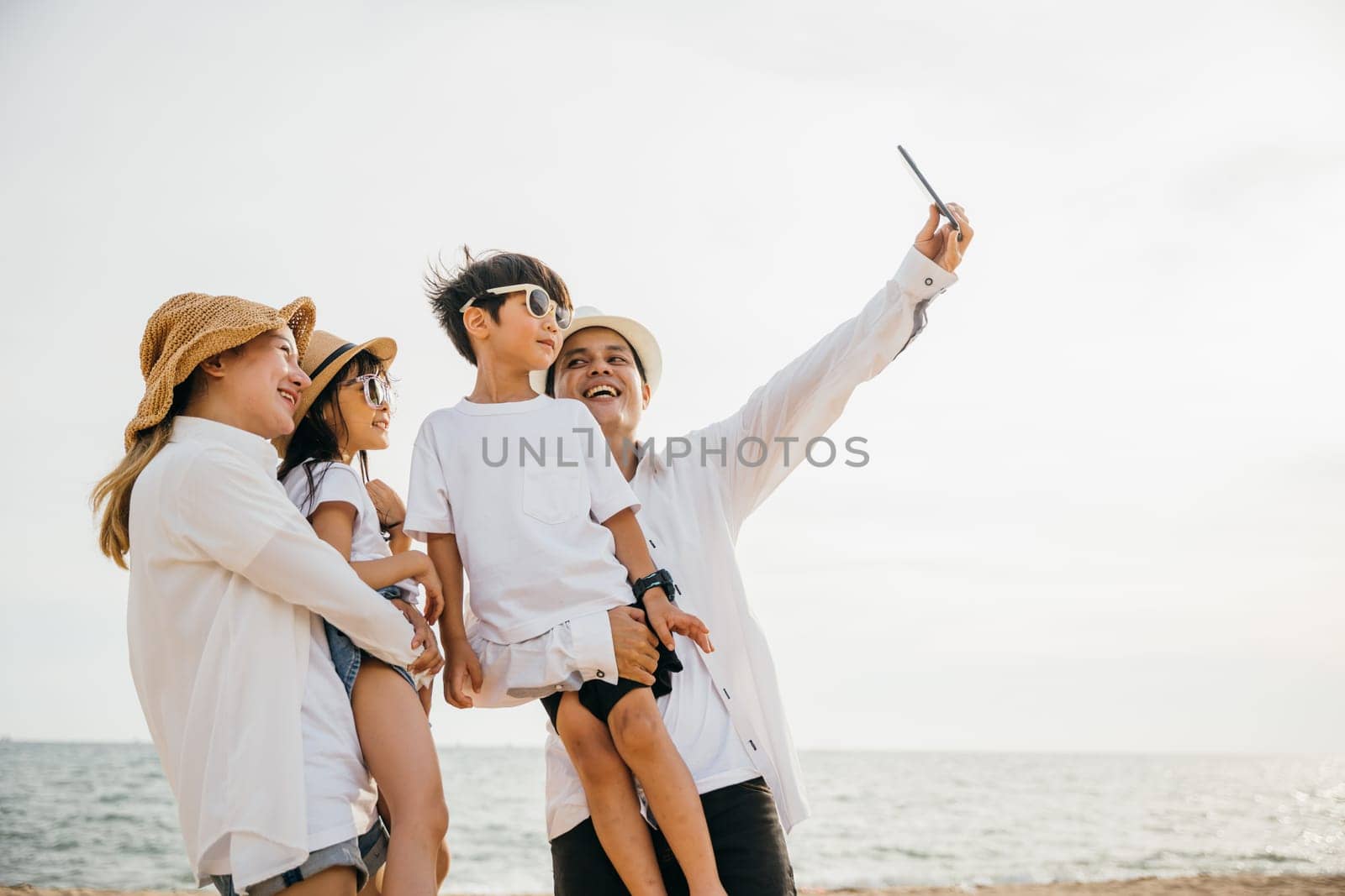 Beachside family fun as they take a cheerful selfie together near the sea. Laughter and joy unfold creating a playful and memorable moment of togetherness during a summer travel adventure.