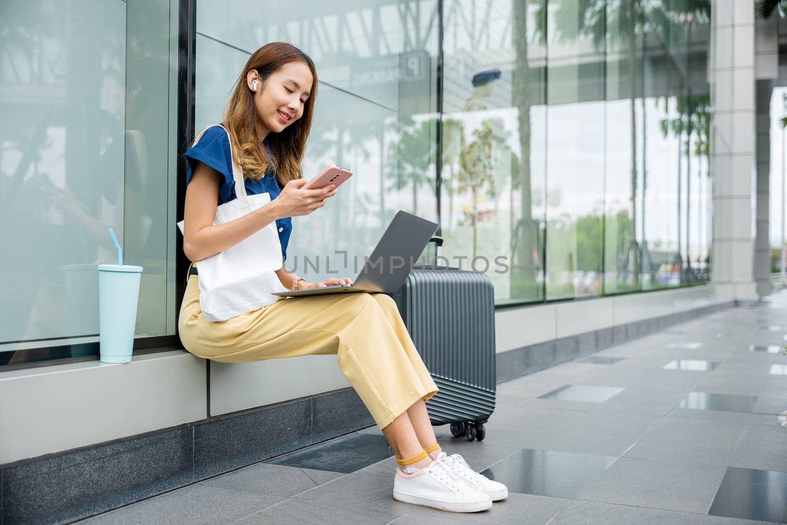 A girl works remotely from a train station, with her laptop and luggage beside her by Sorapop