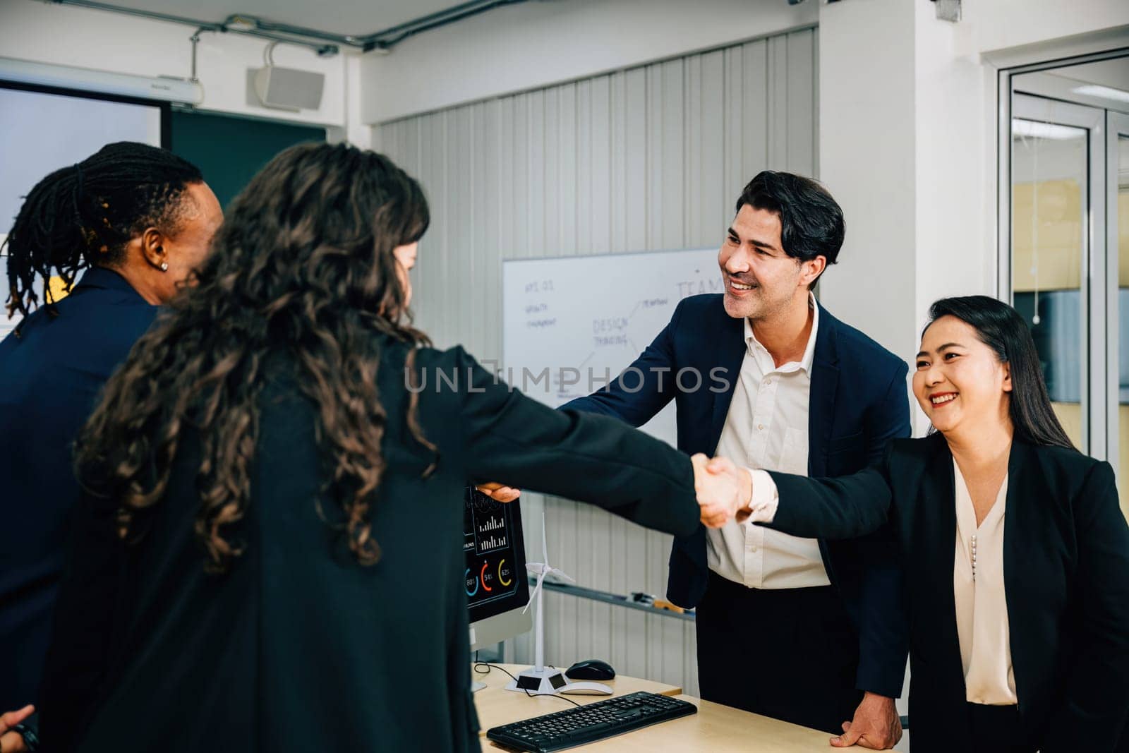 In a meeting, business people shake hands in an office, signifying their successful partnership. Colleagues, including managers, lawyers, and executives, celebrate their achievement. Teamwork