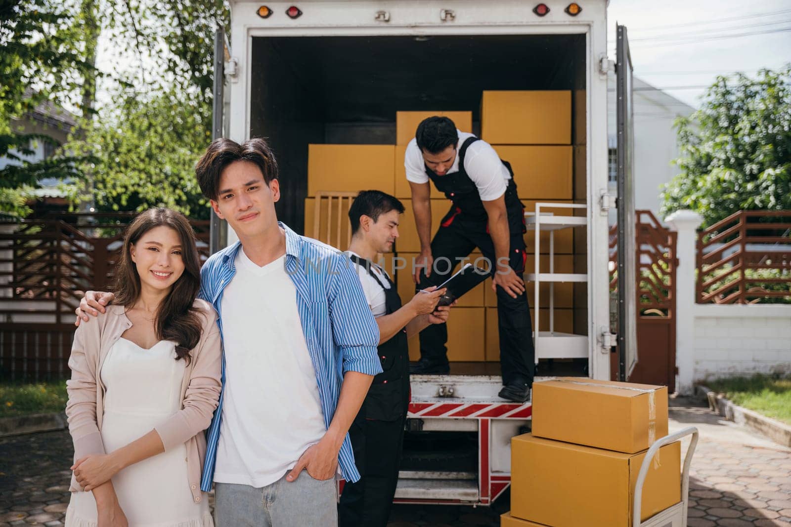 Captured in a portrait a smiling couple watches professional movers load furniture onto a truck for relocation. Quality service and teamwork for happy customers. Moving Day Concept