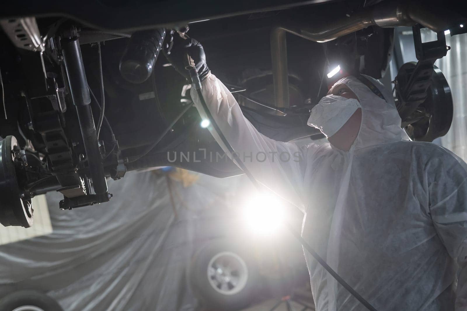The master sprays an anti-corrosion compound on the bottom of the car