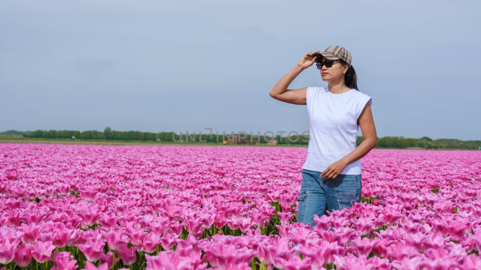 A woman stands gracefully in a field of vibrant pink tulips, surrounded by natures beauty in Texel, Netherlands by fokkebok