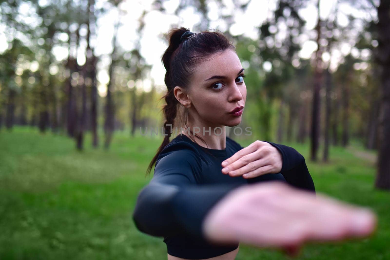 A young woman in a black training clothing holds her arms in a fighting pose for battle in the forest. by Nickstock