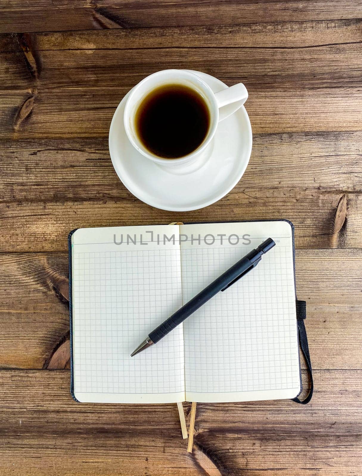 Coffee in a cup and a notepad with a pen, top view. Vertical photo. Coffee in a cup with a saucer and a notebook with a pen on a wooden table.