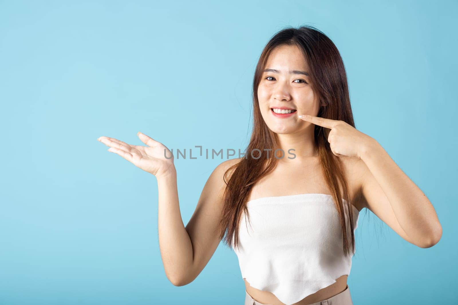 Young woman pointing to strong white teeth and open hand palm for display product by Sorapop