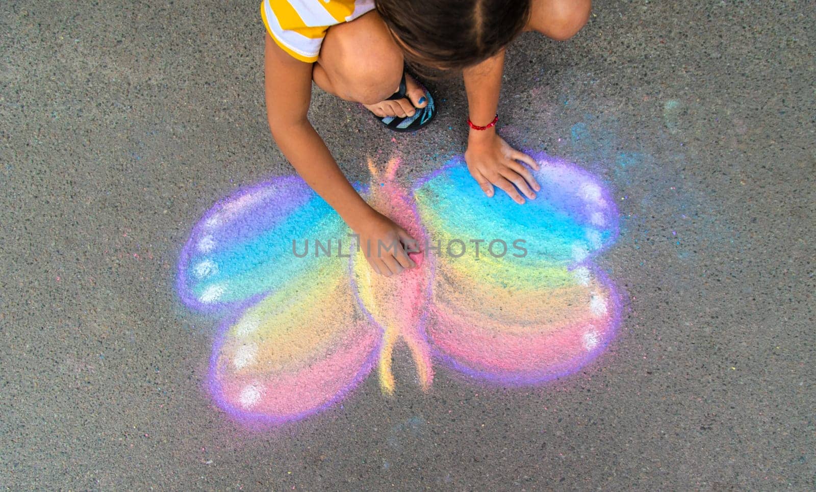 A child draws a butterfly on the asphalt with chalk. Selective focus. Kid.