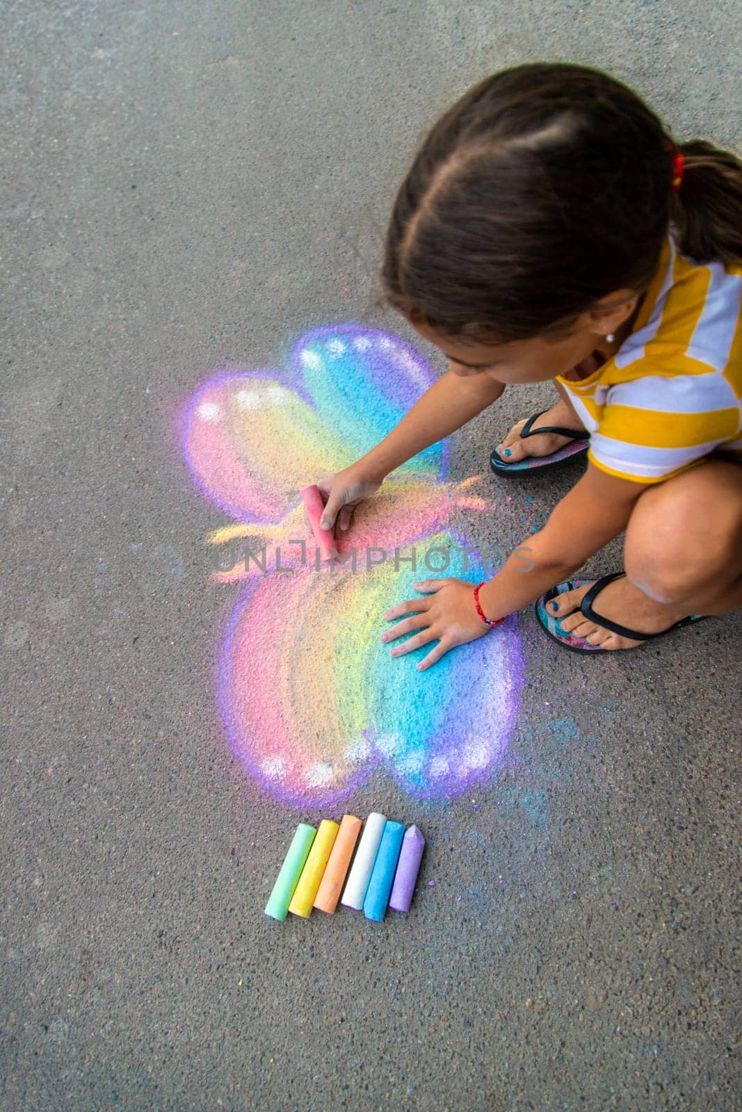 A child draws a butterfly on the asphalt with chalk. Selective focus. Kid.