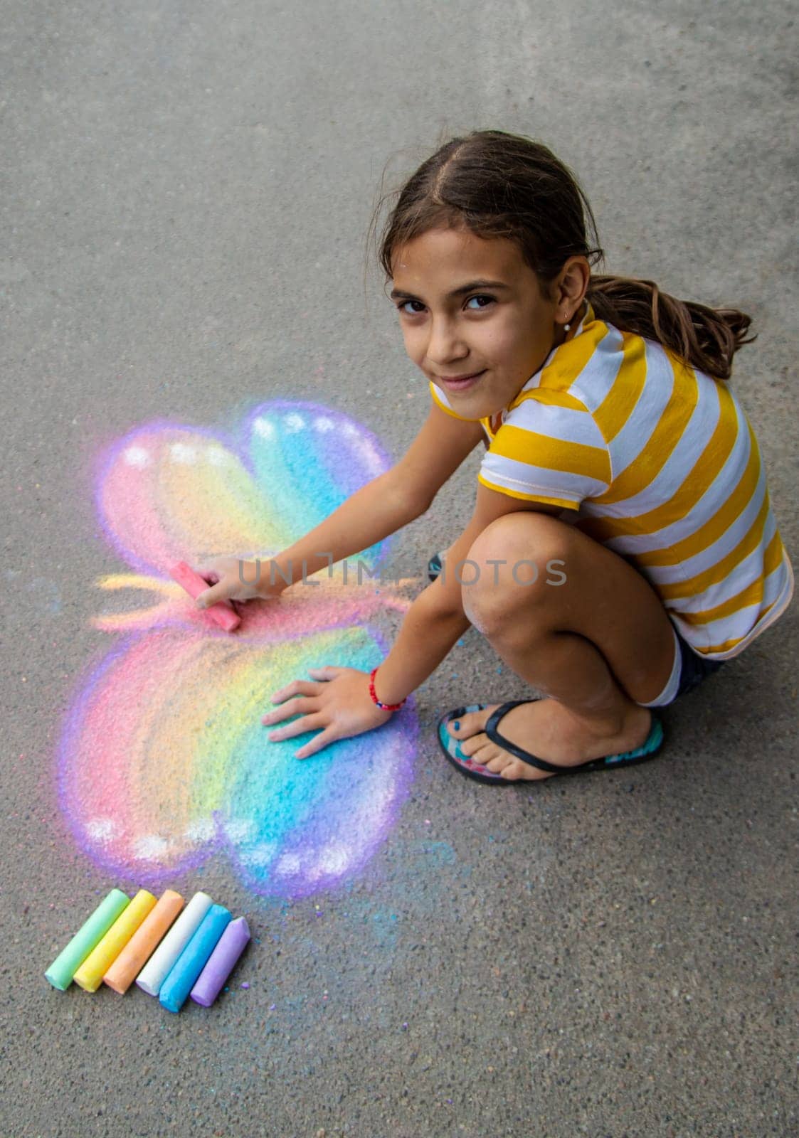 A child draws a butterfly on the asphalt with chalk. Selective focus. Kid.