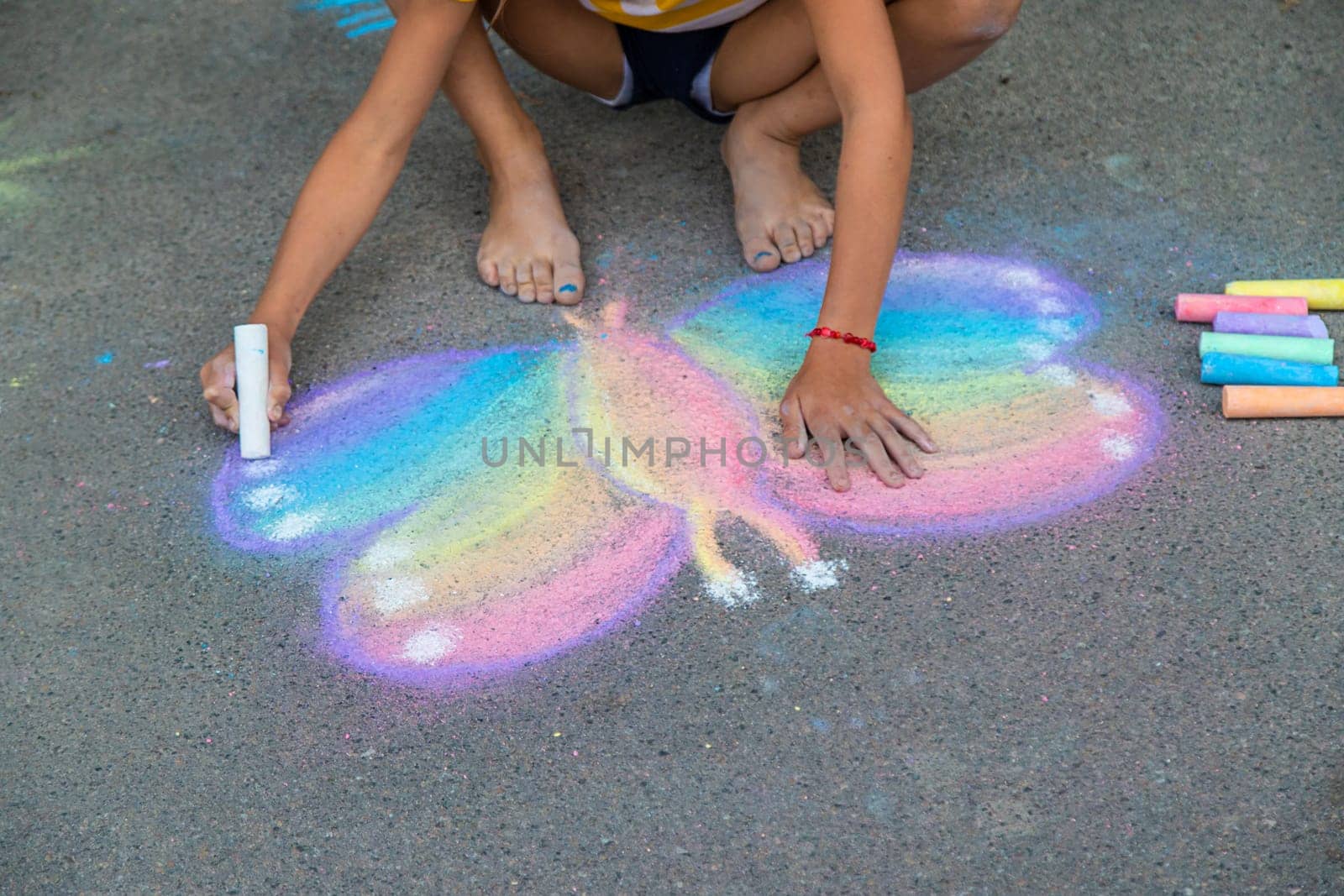 A child draws a butterfly on the asphalt with chalk. Selective focus. Kid.