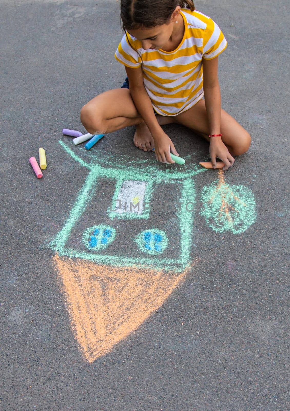 A child draws a house on the asphalt with chalk. Selective focus. Kid.