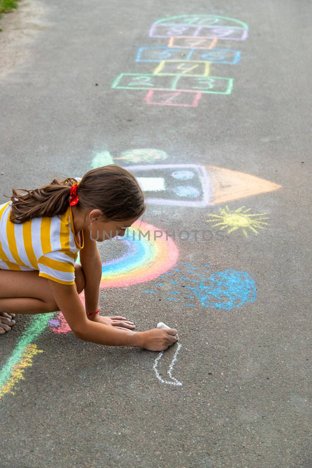 A child draws a house and a rainbow on the asphalt with chalk. Selective focus. Kid.