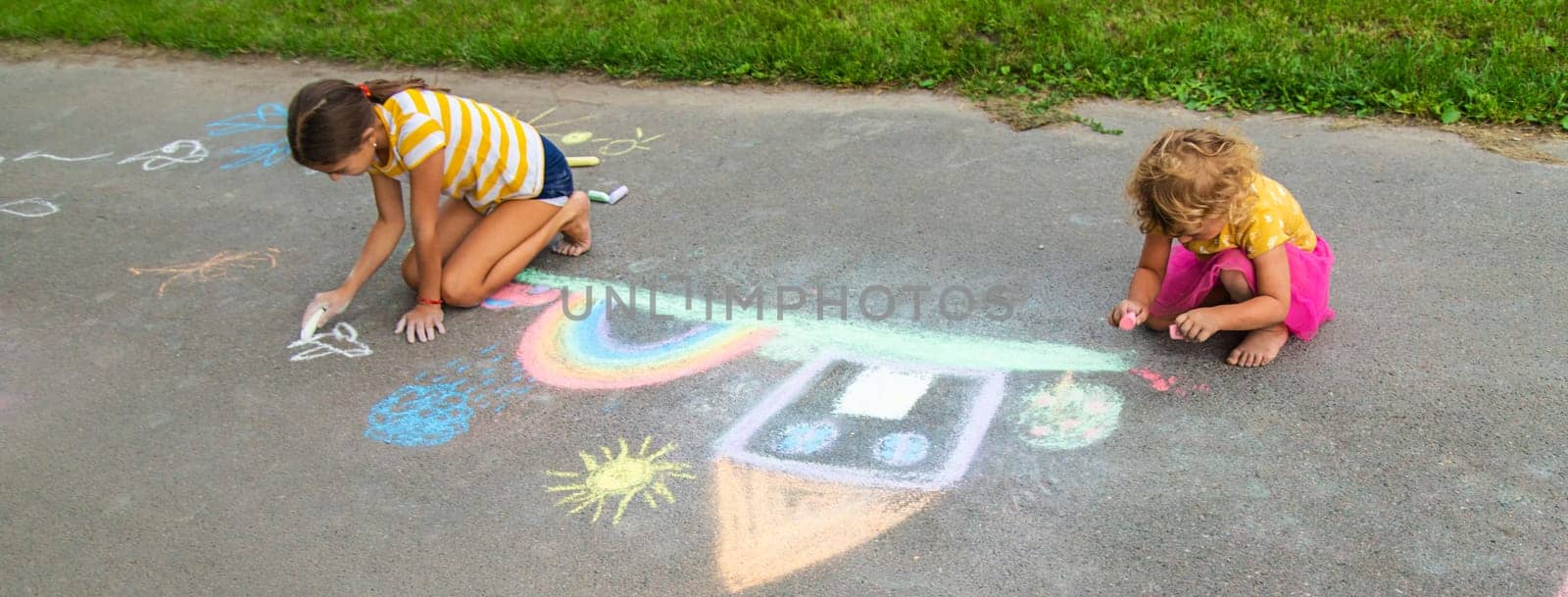 A child draws a house and a rainbow on the asphalt with chalk. Selective focus. by yanadjana