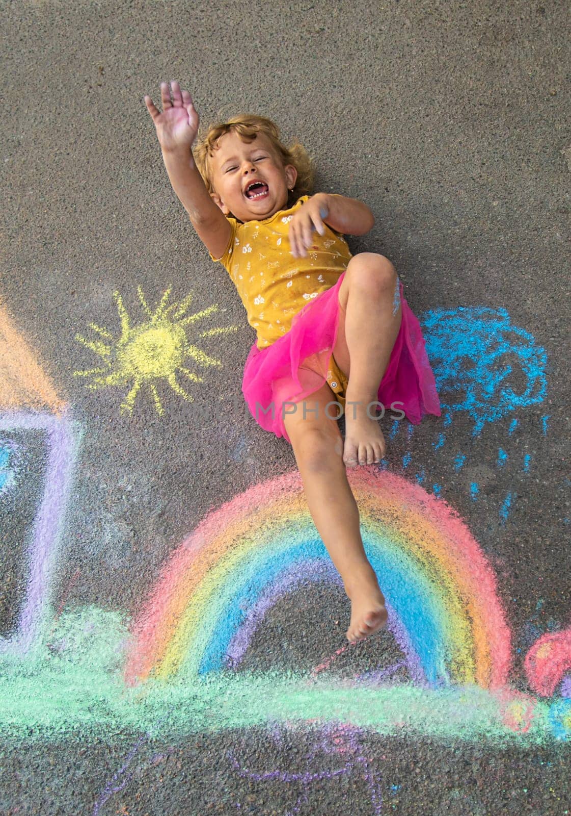 A child draws a house and a rainbow on the asphalt with chalk. Selective focus. Kid.