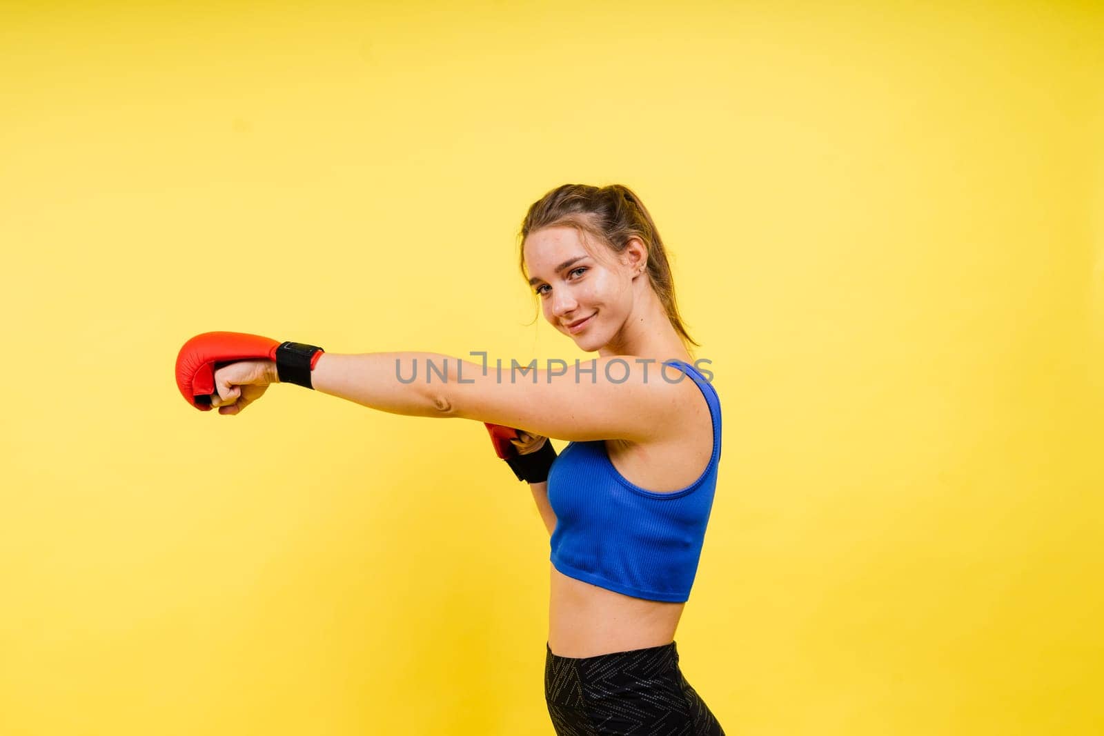 Woman boxer in gloves training on a grey and yellow background studio
