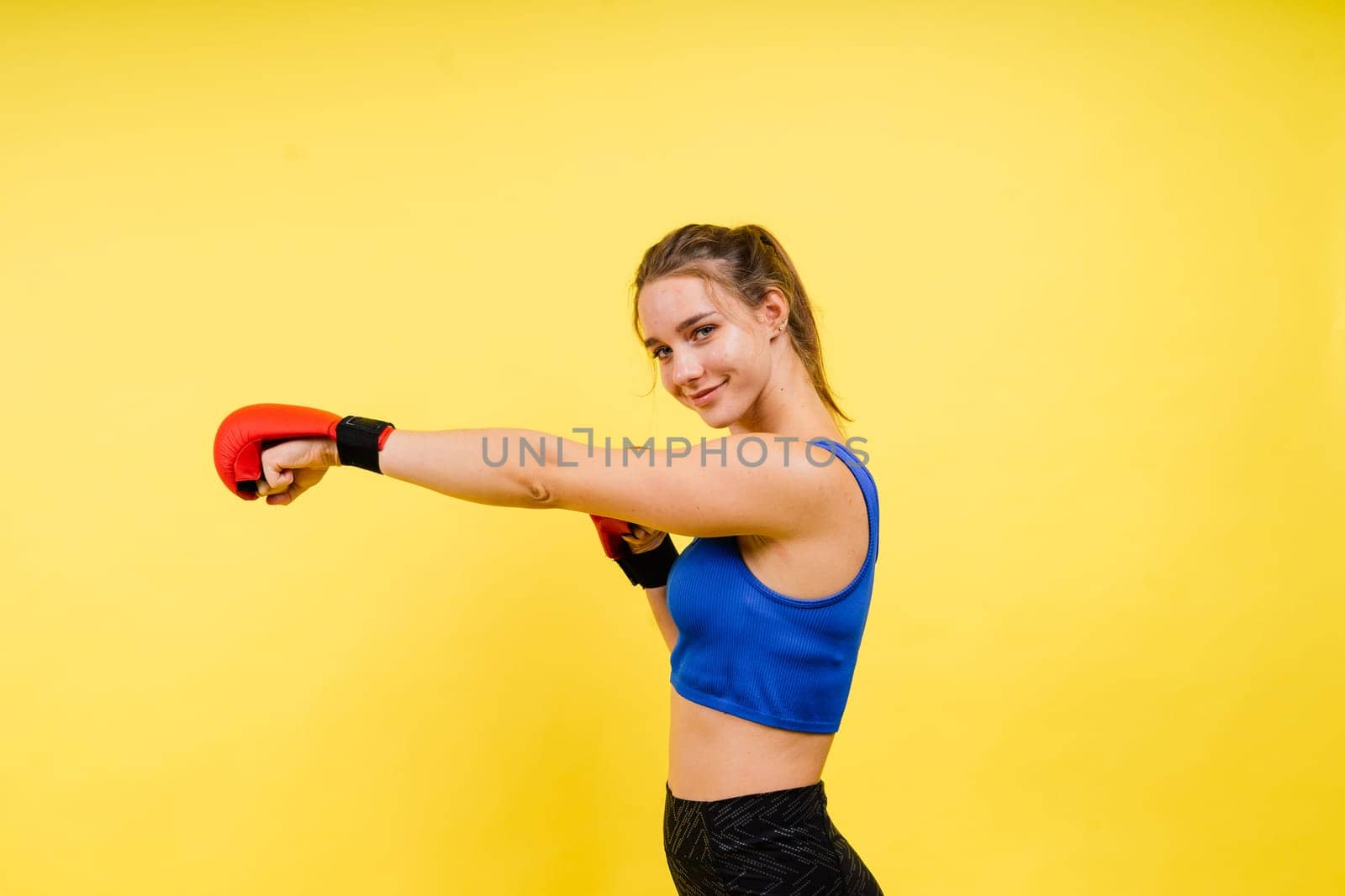 Woman boxer in gloves training on grey and yellow background studio by Zelenin