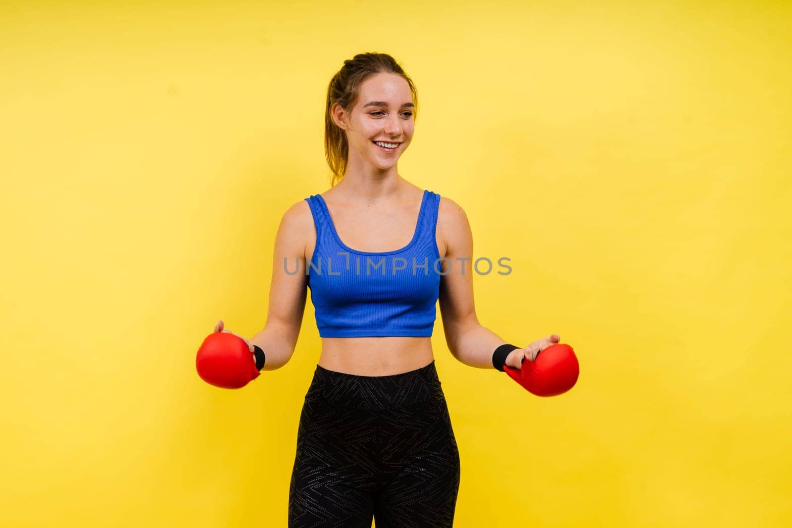 Woman boxer in gloves training on grey and yellow background studio by Zelenin