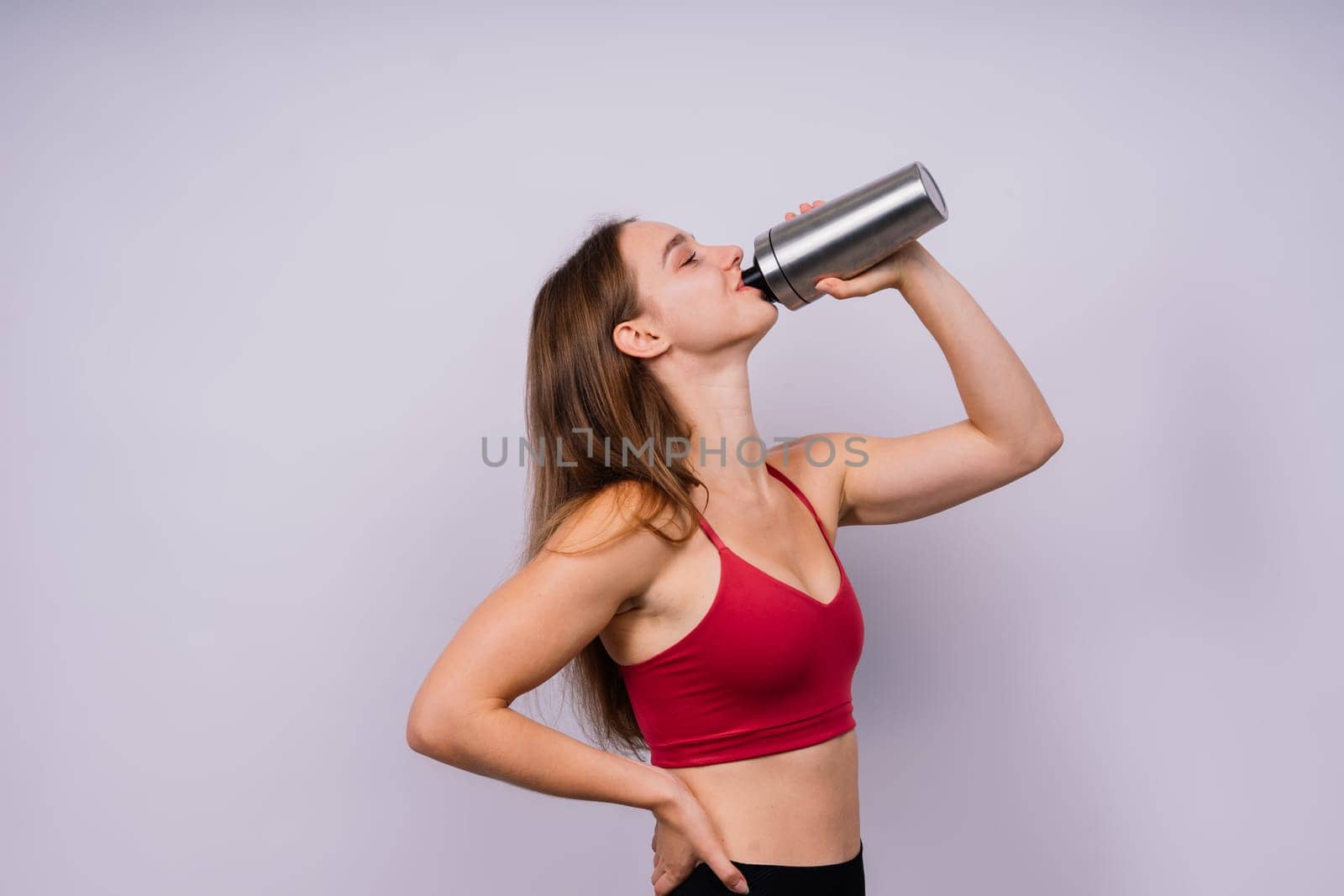 Sporty muscular woman drinking water, isolated against a white background
